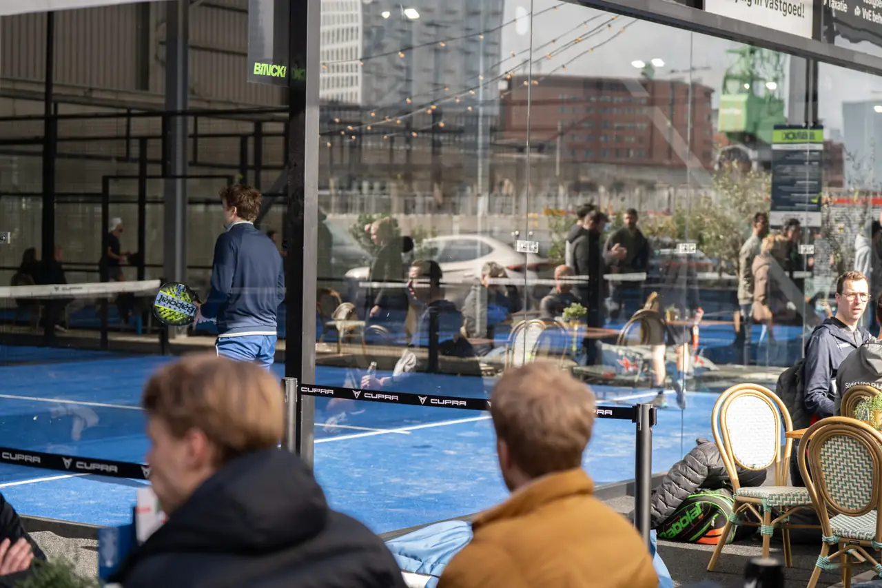 Spelers aan de bar van Binck Padel in Den Haag, met zicht op de banen